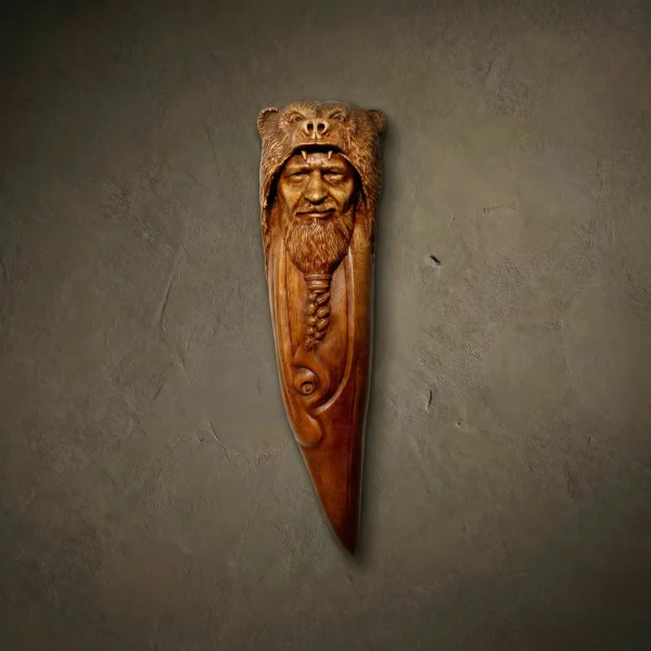 A luxury vertical wood carving of a Norse shaman wearing a grizzly bear headdress. The piece features a detailed bearded face with braided hair peeking through the bear's open jaws. The lower section transitions into elegant Celtic knotwork and serpentine scrolls. Hand-crafted with high-relief textures and a natural, light-oak satin finish.