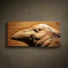 Custom hand-carved Iroko wood relief sculpture of a Raven's head. This detailed wildlife carving captures the intelligent expression and layered feather textures of the raven in profile, finished with natural oil to highlight the deep, warm wood grain. A striking example of bespoke bird-themed wall art and custom-made animal carvings available for order.