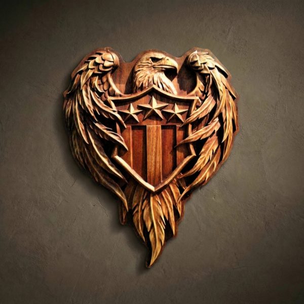 Shaped 3D wood relief carved from Iroko. Features a majestic Bald Eagle with outspread wings holding a shield with three stars and vertical stripes. Solid wood with detailed feather textures, natural grain, and oil finish.