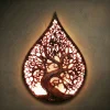 Teardrop-shaped wall lamp hand-carved from solid Iroko hardwood, featuring the Norse Yggdrasil Tree of Life. The design uses intricate openwork carving to allow light to shine through the branches, creating a mystical glow. High-relief details on the twisted trunk and sprawling canopy. Hand-finished with natural oils to highlight the rich, warm grain of the Iroko wood. A functional masterpiece of pagan decor and spiritual lighting for luxury interiors.